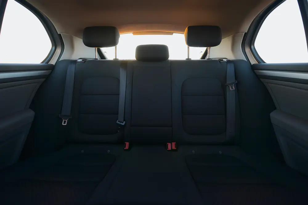 La imagen muestra el interior de un coche taxi con posibilidad de tres plaza. El espacio está limpio y los asientos con reposa cabezas son en color gris muy oscuro, se observa igualmente los cinturones de seguridad y los anclajes en color rojo.